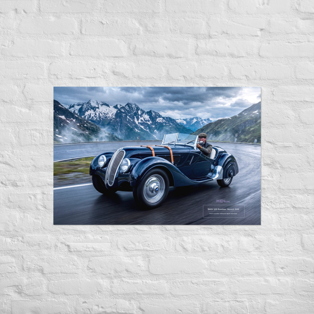 A rectangular wall art print showing a vintage dark blue convertible car driving along a mountain road, mounted on a white painted brick wall.