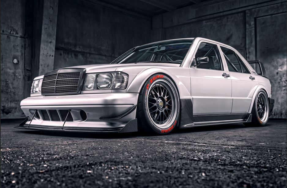 A heavily customized white Mercedes-Benz sedan with a widebody kit, custom front and rear bumpers, and multi-spoke wheels with red accents, parked inside a dark concrete garage.